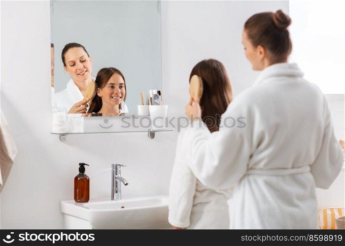 beauty, hygiene, morning and people concept - happy smiling mother and daughter with hairbrush brushing hair at bathroom. mother and daughter brushing hair at bathroom