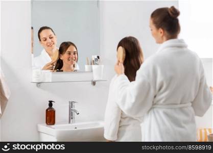 beauty, hygiene, morning and people concept - happy smiling mother and daughter with hairbrush brushing hair at bathroom. mother and daughter brushing hair at bathroom