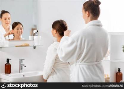 beauty, hygiene, morning and people concept - happy smiling mother and daughter looking to mirror and braiding hair at bathroom. mother and daughter braiding hair at bathroom