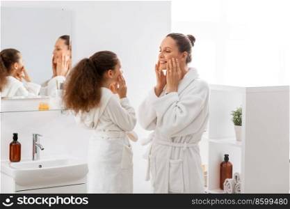 beauty, hygiene, morning and people concept - happy smiling mother and daughter touching their faces in bathroom. mother and daughter touching faces in bathroom