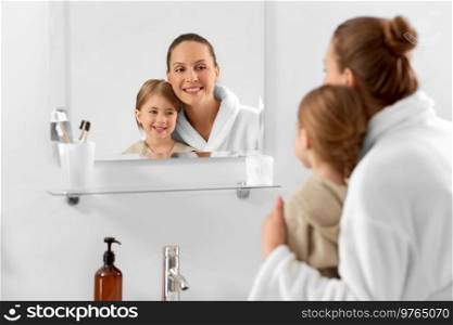 beauty, hygiene, morning and people concept - happy smiling mother and daughter looking to mirror in bathroom. mother and daughter looking to mirror in bathroom