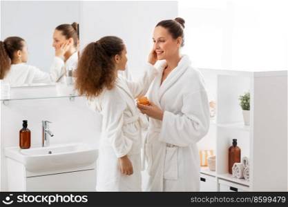 beauty, hygiene, morning and people concept - happy smiling mother and daughter with moisturizer at bathroom. mother and daughter with moisturizer at bathroom