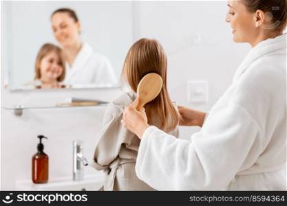 beauty, hygiene, morning and people concept - happy smiling mother and little daughter with hairbrush brushing hair at bathroom. mother and daughter brushing hair at bathroom