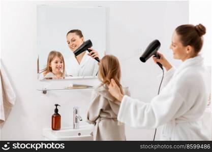beauty, hygiene, morning and people concept - happy smiling mother and little daughter with hair dryer at bathroom. mother and daughter drying hair at bathroom