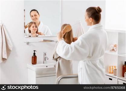 beauty, hygiene, morning and people concept - happy smiling mother and little daughter with hairbrush brushing hair at bathroom. mother and daughter brushing hair at bathroom