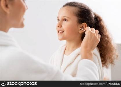 beauty, hygiene, morning and people concept - happy smiling mother cleaning daughter’s ear with cotton swab in bathroom. happy mother cleaning daughter’s ear in bathroom