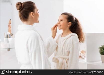 beauty, hygiene, morning and people concept - happy smiling mother with cotton pad cleaning daughter’s face skin at bathroom. mother with cotton pad cleaning daughter’s face