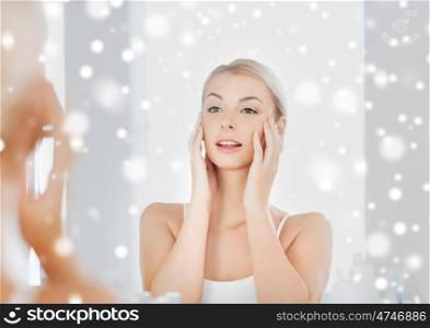 beauty, hygiene, morning and people concept - smiling young woman looking to mirror at home bathroom over snow