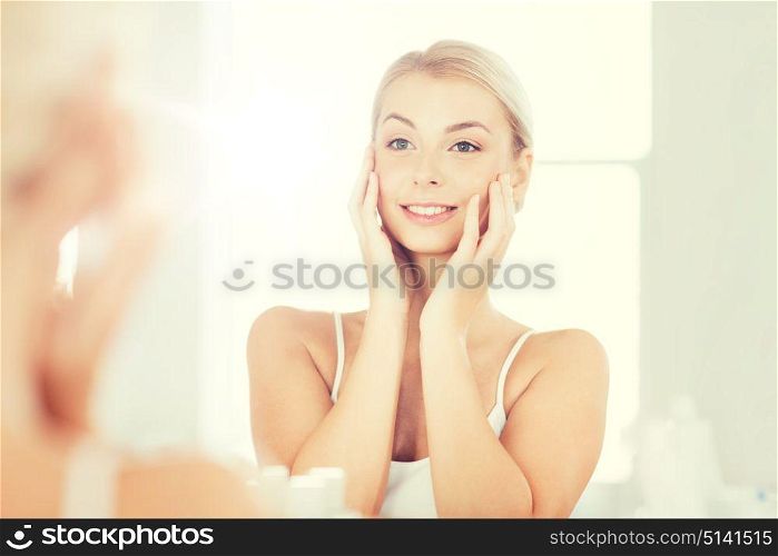 beauty, hygiene, morning and people concept - smiling young woman looking to mirror at home bathroom. happy young woman looking to mirror at bathroom