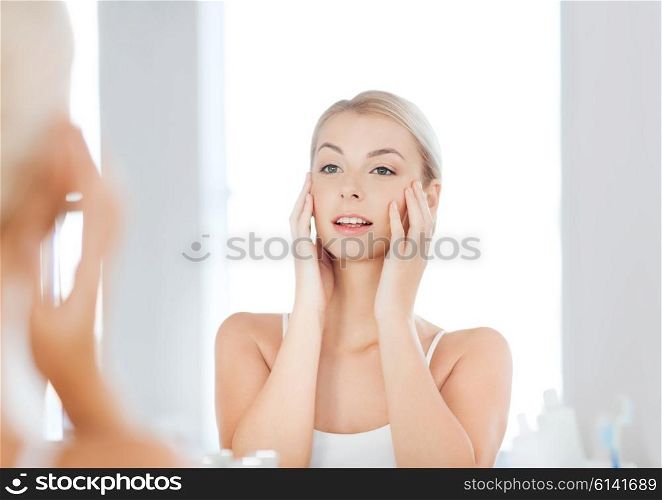 beauty, hygiene, morning and people concept - smiling young woman looking to mirror at home bathroom