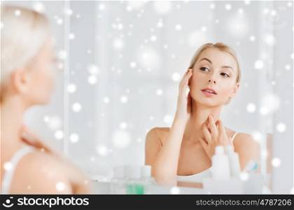 beauty, hygiene, morning and people concept - young woman looking to mirror at home bathroom over snow