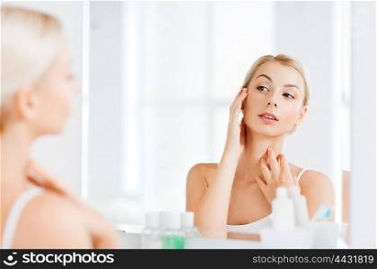beauty, hygiene, morning and people concept - young woman looking to mirror at home bathroom