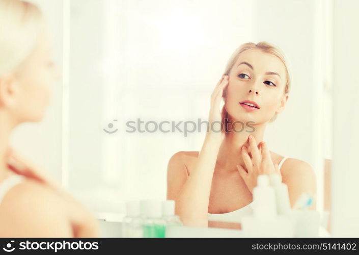 beauty, hygiene, morning and people concept - young woman looking to mirror at home bathroom. happy young woman looking to mirror at bathroom