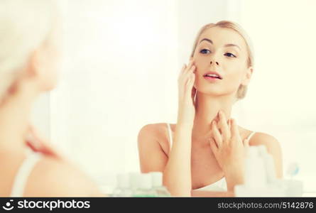 beauty, hygiene, morning and people concept - young woman looking to mirror at home bathroom. happy young woman looking to mirror at bathroom