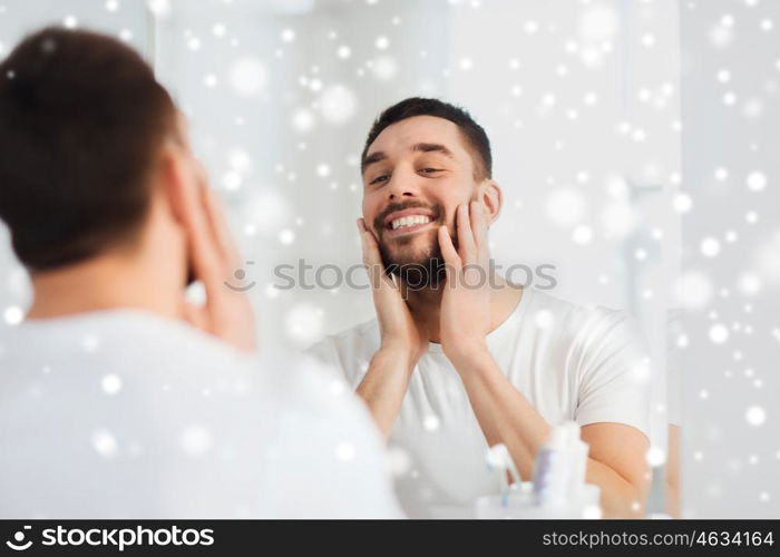 beauty, hygiene, shaving and people concept - smiling young man looking to mirror at home bathroom over snow