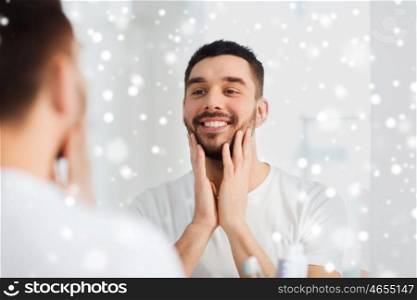 beauty, hygiene, shaving and people concept - smiling young man looking to mirror at home bathroom over snow