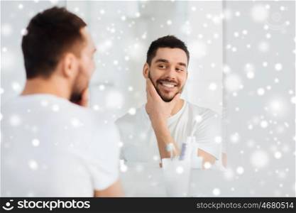 beauty, hygiene, shaving and people concept - smiling young man looking to mirror at home bathroom over snow