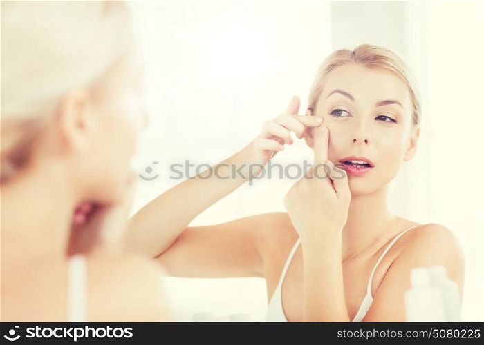 beauty, hygiene, skin problem and people concept - young woman looking to mirror and squeezing pimple at home bathroom. woman squeezing pimple at bathroom mirror