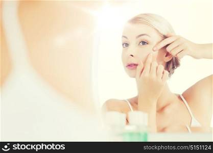 beauty, hygiene, skin problem and people concept - young woman looking to mirror and squeezing pimple at home bathroom. woman squeezing pimple at bathroom mirror