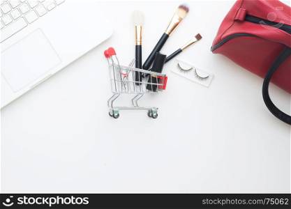 Beauty items and cosmetics in shopping cart with laptop computer on white background, Online shopping