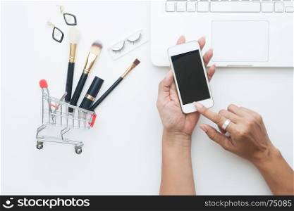Beauty items, Brushes set in shopping cart with woman hand holding mobile phone, Top view shopping online concept