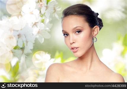beauty, jewelry, accessories, people and luxury concept - close up of beautiful asian woman face with earring over natural spring cherry blossom background