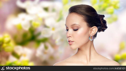 beauty, jewelry, accessories, people and luxury concept - close up of beautiful asian woman face with earring over natural spring lilac blossom background