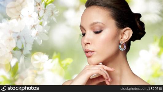beauty, jewelry, accessories, people and luxury concept - close up of beautiful asian woman face with earring over natural spring cherry blossom background