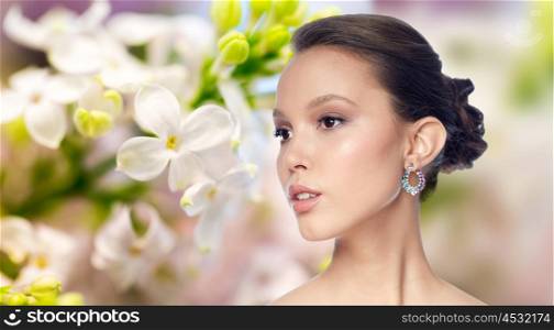 beauty, jewelry, accessories, people and luxury concept - close up of beautiful asian woman face with earring over natural spring lilac blossom background