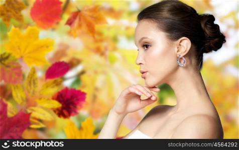 beauty, jewelry, accessories, people and luxury concept - close up of beautiful asian woman face with earring over autumn leaves background