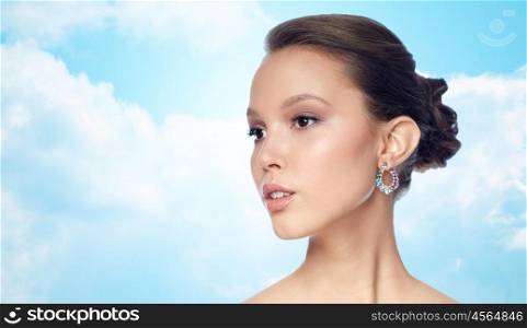 beauty, jewelry, accessories, people and luxury concept - close up of beautiful asian woman face with earring over blue sky and clouds background