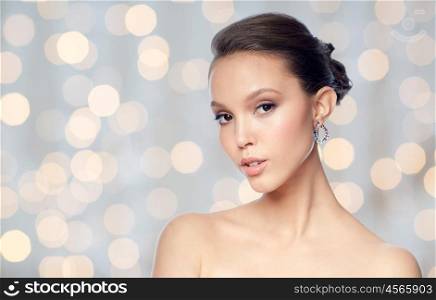 beauty, jewelry, accessories, people and luxury concept - close up of beautiful asian woman face with earring over holidays lights background