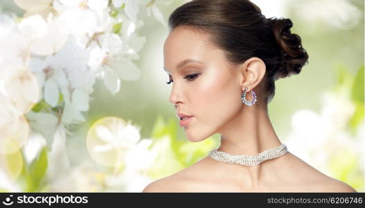 beauty, jewelry, accessories, people and luxury concept - close up of beautiful asian woman face with earring over natural spring cherry blossom background