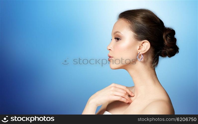 beauty, jewelry, accessories, people and luxury concept - close up of beautiful asian woman face with earring over blue background