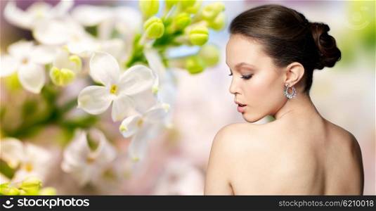 beauty, jewelry, accessories, people and luxury concept - close up of beautiful asian woman face with earring over natural spring lilac blossom background