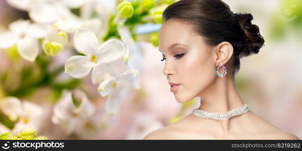 beauty, jewelry, accessories, people and luxury concept - close up of beautiful asian woman face with earring over natural spring lilac blossom background