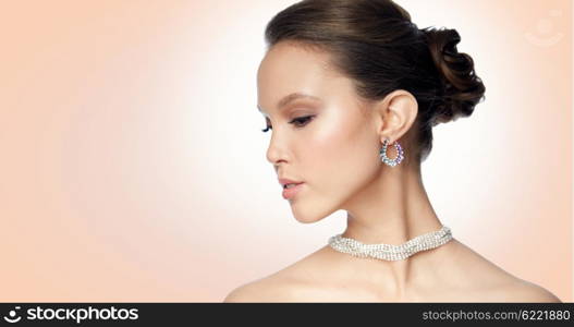 beauty, jewelry, accessories, people and luxury concept - close up of beautiful asian woman face with earring over beige background