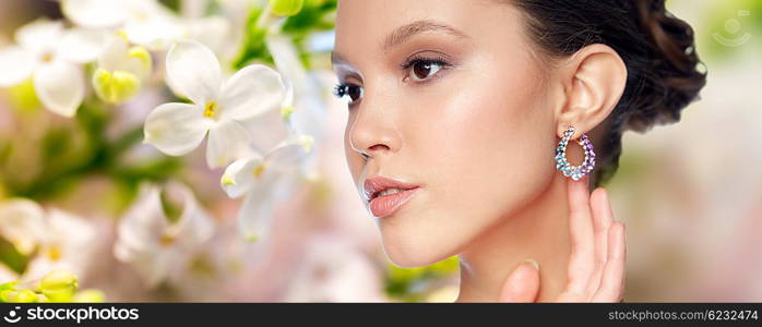 beauty, jewelry, accessories, people and luxury concept - close up of beautiful asian woman face with earring over natural spring lilac blossom background