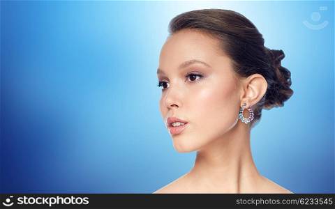 beauty, jewelry, accessories, people and luxury concept - close up of beautiful asian woman face with earring over blue background