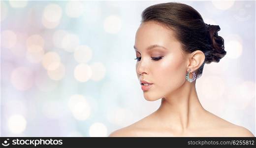 beauty, jewelry, accessories, people and luxury concept - close up of beautiful asian woman face with earring over blue holidays lights background