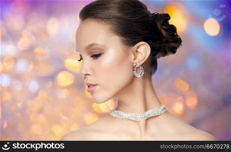 beauty, jewelry, accessories, people and luxury concept - close up of beautiful asian woman face with earring over holidays lights background. close up of beautiful woman face with earring. close up of beautiful woman face with earring