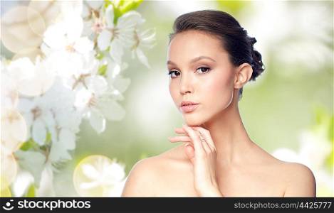 beauty, jewelry, accessories, people and luxury concept - face of beautiful young asian woman with golden ring over natural spring cherry blossom background