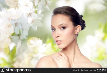 beauty, jewelry, accessories, people and luxury concept - face of beautiful young asian woman with golden ring over natural spring cherry blossom background