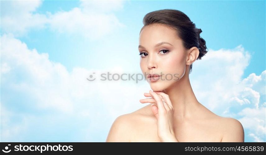 beauty, jewelry, accessories, people and luxury concept - face of beautiful young asian woman with golden ring over blue sky and clouds background