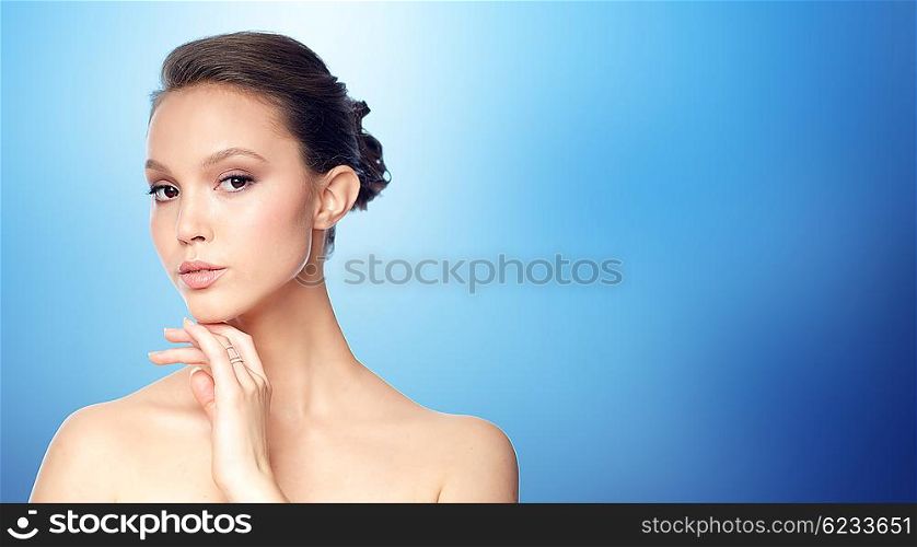 beauty, jewelry, accessories, people and luxury concept - face of beautiful young asian woman with golden ring over blue background