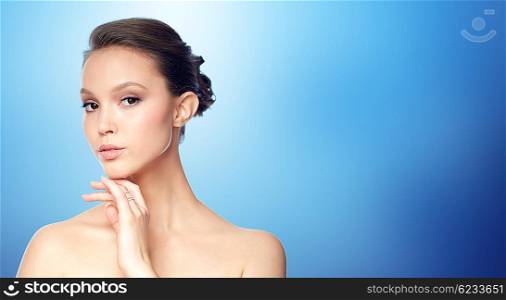 beauty, jewelry, accessories, people and luxury concept - face of beautiful young asian woman with golden ring over blue background