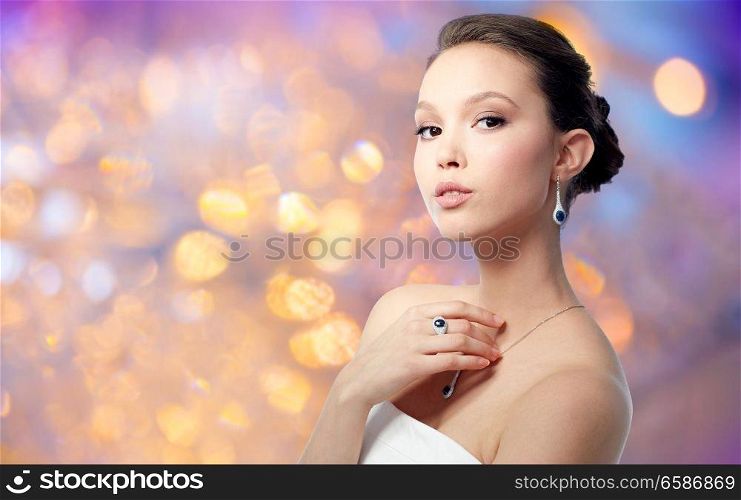 beauty, jewelry and luxury concept - beautiful asian woman or bride with earring, finger ring and pendant over holidays lights background. beautiful woman with earring, ring and pendant