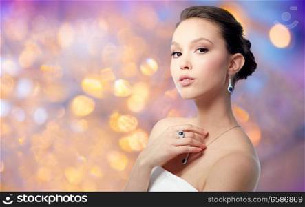 beauty, jewelry and luxury concept - beautiful asian woman or bride with earring, finger ring and pendant over holidays lights background. beautiful woman with earring, ring and pendant