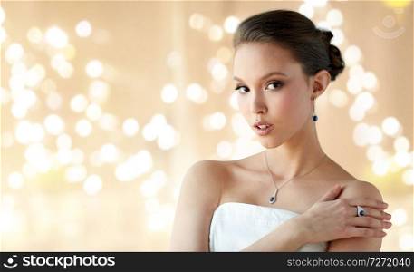 beauty, jewelry and luxury concept - beautiful asian woman or bride with diamond earring, finger ring and pendant over beige background and festive lights. beautiful woman with earring, ring and pendant