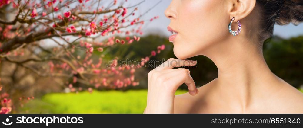 beauty, jewelry and luxury concept - close up of beautiful woman face with earring over natural spring cherry blossom background. close up of beautiful woman face with earring. close up of beautiful woman face with earring